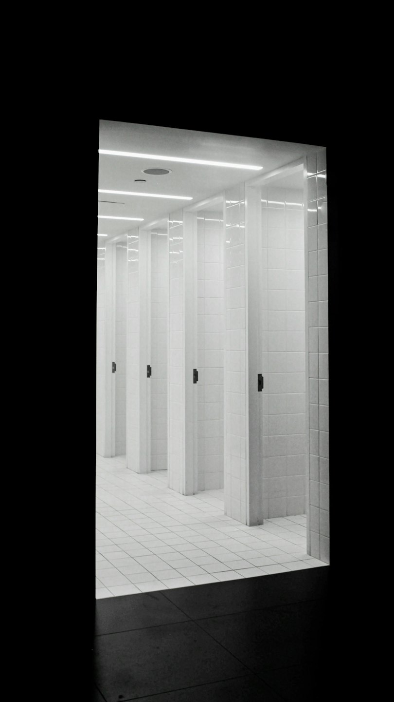 Row of clean white tiled stalls in a public restroom.