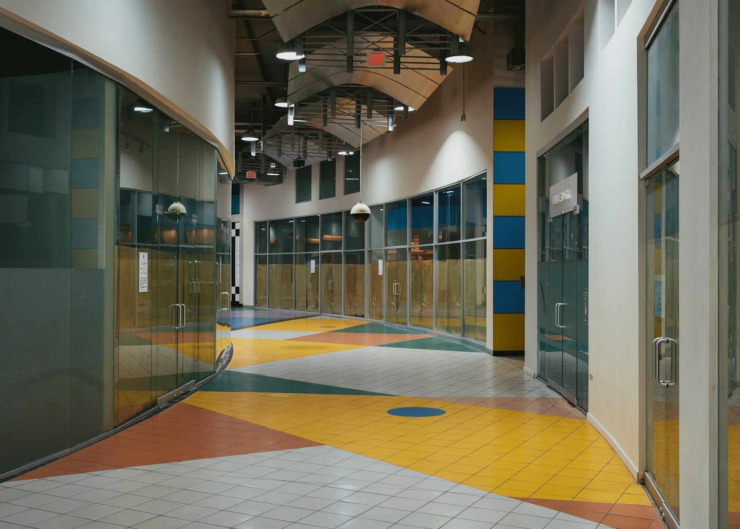 Empty commercial hallway with patterned tile flooring and vacant storefronts.
