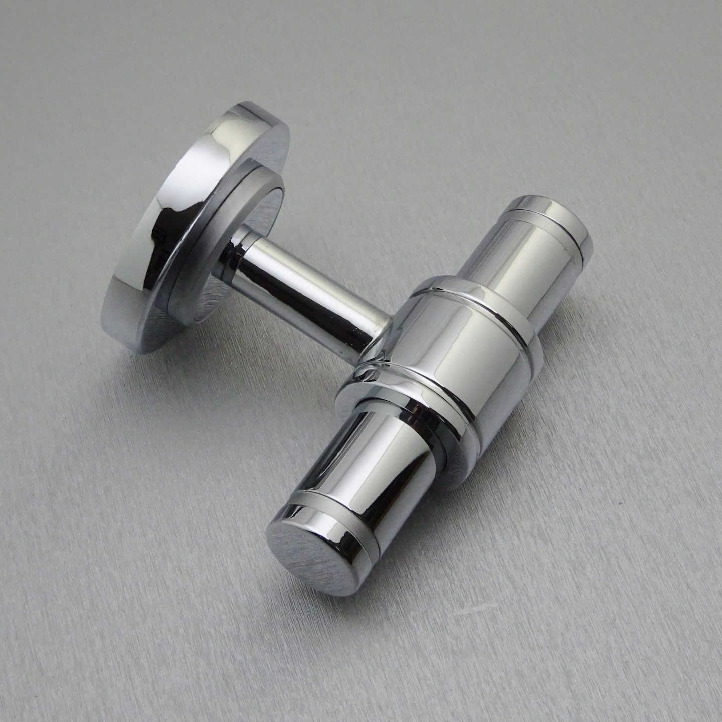 Chrome pipe connector resting on a brushed metal surface.